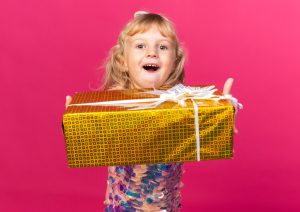 excited little blonde girl holding gift box isolated pink wall with copy space - Правила этикета для детей в любых жизненных ситуациях