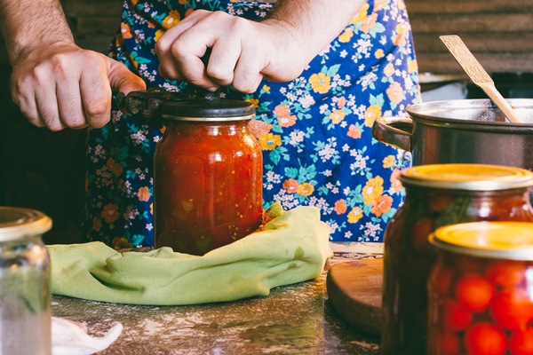 a man in a colored apron clogs tomatoes and lecho sauce in glass jars in a farmhouse - Лечо двухцветное с душистыми травами