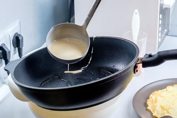 batter pouring out of a metal bucket onto a redhot greased frying pan the process of baking pancakes traditional treat for the holiday of maslenitsa - Изделия из теста: полезные советы