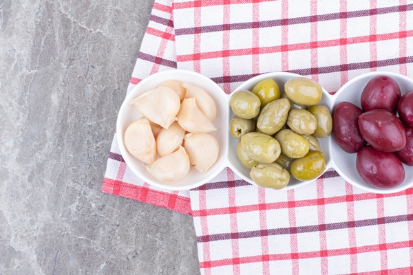 bowls of pickled plums olives and garlic on tablecloth - Острый маринованный чеснок