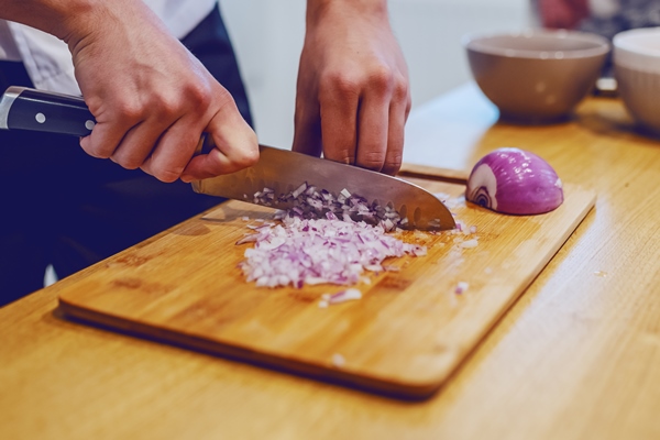 caucasian chef in uniform standing at domestic kitchen and chopping onion - Шанежки на кефире с картошкой