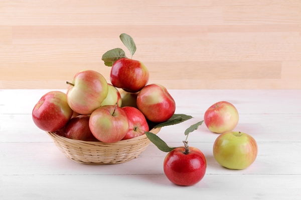 fresh ripe red apples with leaves in a basket on a white wooden table and on a background of natural wood - Клюквенный зефир