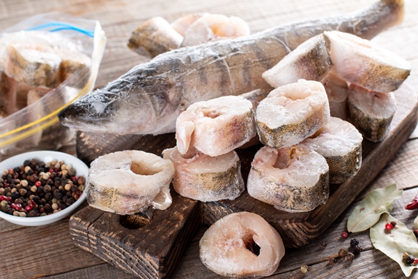 frozen fish on a cutting board on a wooden table frozen food - Как правильно обрабатывать и готовить рыбу?