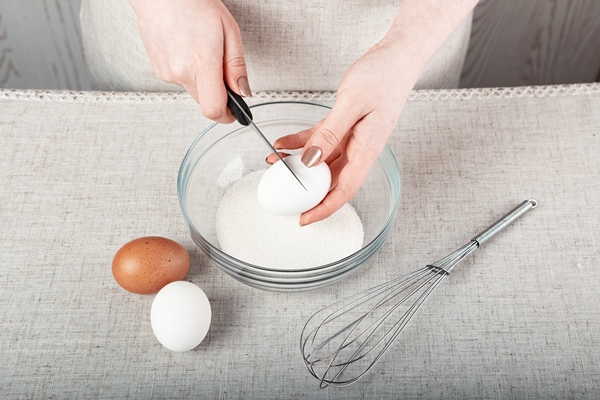 hands breaking an egg with a knife over a glass bowl of sugar - Низкокалорийная творожная пасха
