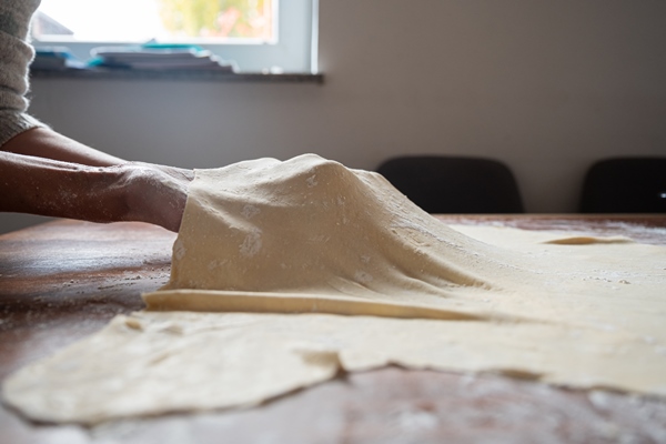 low angle view of a woman stretching rolled homemade vegan pastry dough on domestic dining table - Изделия из теста: полезные советы
