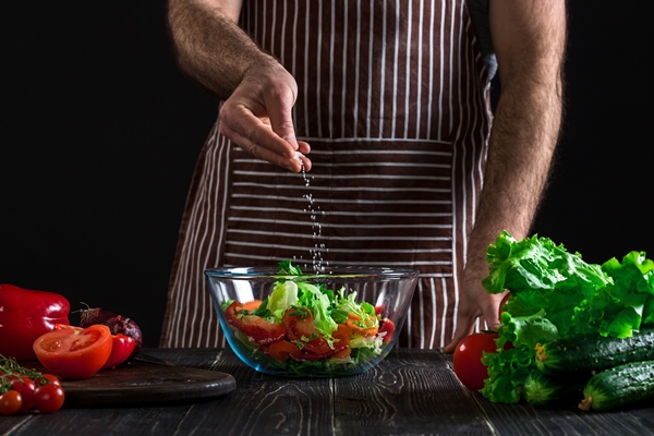 man preparing healthy salad of fresh vegetables on a wooden table on black background vegetarian food healthy or cooking concept - Овощи, бобовые, грибы: полезные советы