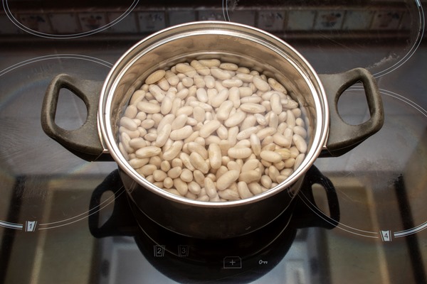 navy beans soaked in water in a stainless steel pot on top of a ceramic hob in a kitchen - Постные котлеты из фасоли