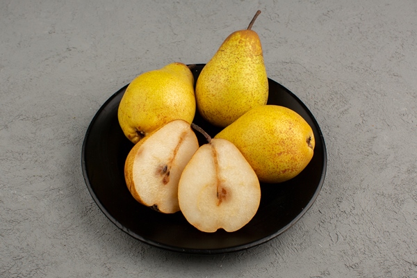 pears ripe sliced and whole inside black plate and on a bright desk - Салат с киви и пекинской капустой