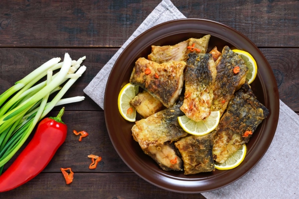 pieces of fried fish carp on a ceramic plate on a dark wooden background top view - Как правильно обрабатывать и готовить рыбу?