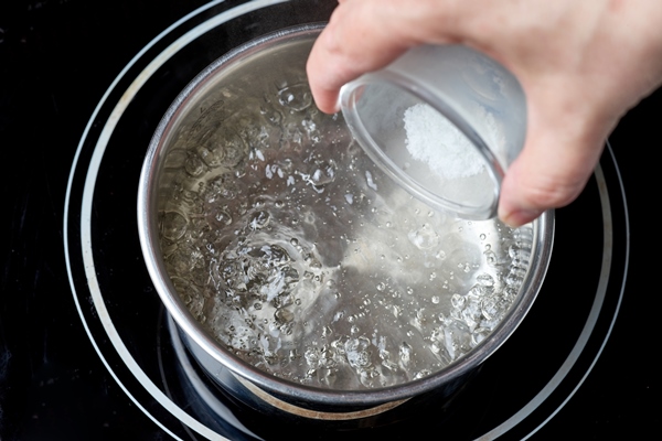 salt is added to boiling water pot on electric induction hob - Острый маринованный чеснок