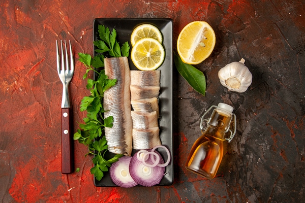 top view fresh sliced fish with greens lemon and onion inside black pan on dark background - Маленькие хитрости приготовления пищи