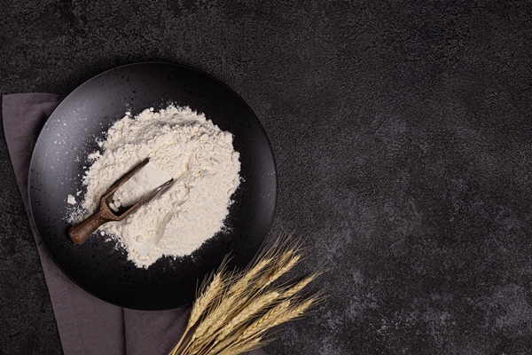 white wheat flour in a wooden spoon on a dark structural background on a plate made of black stone - Постные блинцы на газированной воде