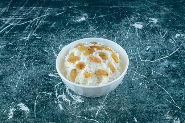 a bowl of rice pudding with raisins on the blue background high quality photo - Постные блинчики с рисом и изюмом
