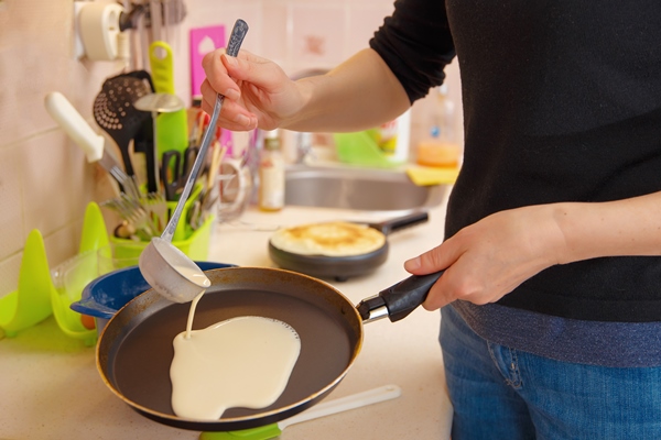 a woman prepares pancakes pours the dough on a hot frying pan holiday maslenitsa - Постные блины с "икрой" из ламинарии