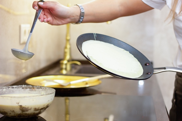 a woman prepares russian pancakes in the kitchen a closeup on a frying pan 1 - Постные гречневые блины с джемом