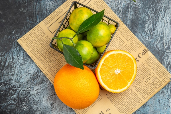 above view of fresh lemons inside and outside of a basket on newspaper on gray background - Постные блинцы с апельсиновым соком