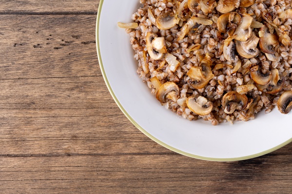 buckwheat porridge with mushrooms in a white plate on wooden background - Постные блинчики с гречкой и грибами