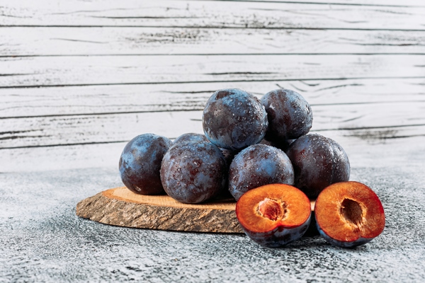 chilly sliced plums in a wooden board on grey stucco background side view - Компот из слив и черноплодной рябины