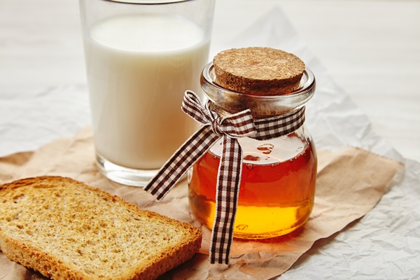closeup of honey jar laced with pretty tape as a gift unfocused glass of milk and dry rye toast bread around everything on craft paper - Постные яблочные блинцы на соевом молоке