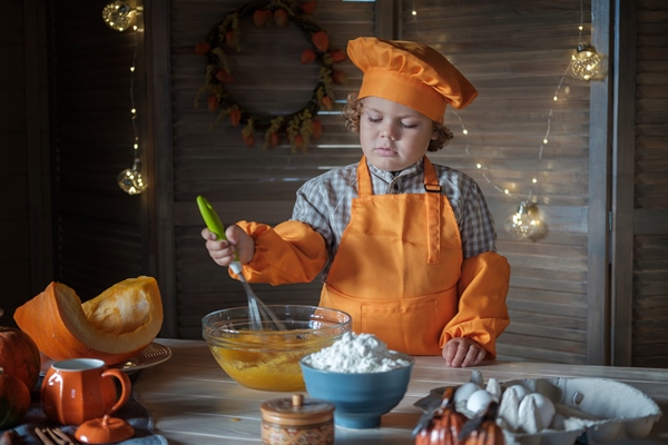 cute curly haired boy in an orange chef costume is preparing pumpkin pie for thanksgiving family holiday traditions 1 - Пасха с тыквой 