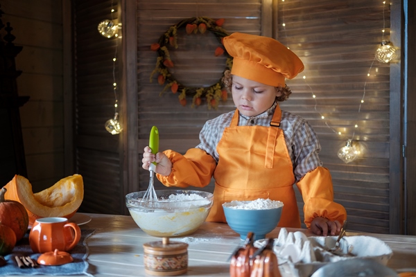 cute curly haired boy in an orange chef costume is preparing pumpkin pie for thanksgiving family holiday traditions - Пасха с тыквой 