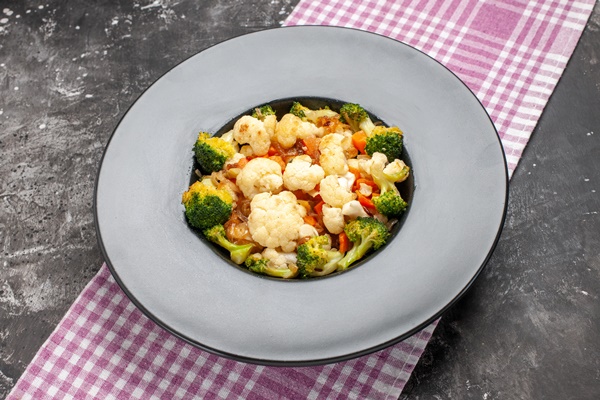 front view broccoli and cauliflower salad on black oval plate pink and white checkered tablecloth on dark background free space - Салат из печёного перца с цветной капустой