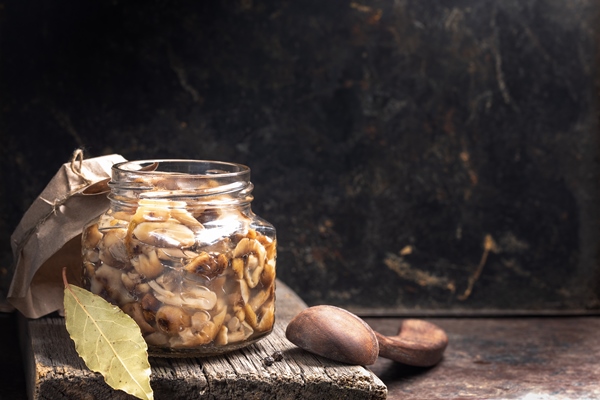 glass jar with pickled mushrooms honey agarics and wooden spoon on old wooden board - Тушёные грибы