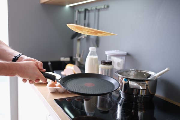 hands hold black iron pan and toss pancake into air - Блины по рецепту семьи Мейендорф № 2