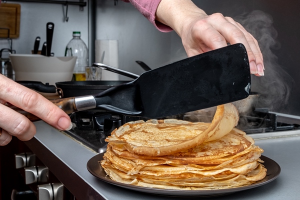 human hands holding a kitchen spatula spread on the dish a freshly baked fragrant pancake from which steam comes home kitchen traditional treat for the holiday of maslenitsa - Постные блинчики с картофельной начинкой