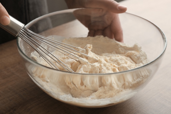 human hands stirring dough with flour in glass bowl on table - Постные блинцы без масла