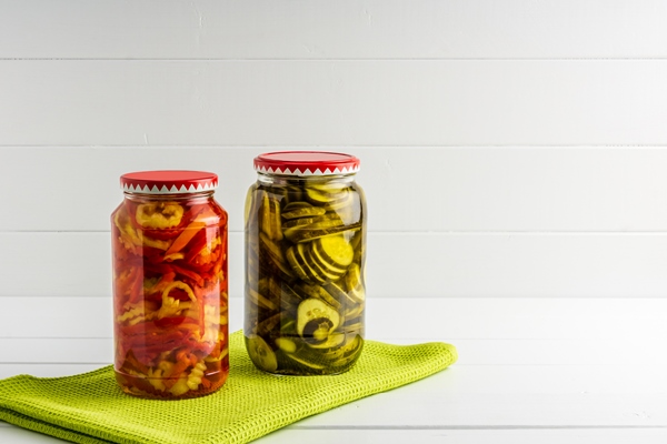 jars with pickled cucumbers and pepper on green cloth white wooden surface background - Медовый перец на зиму