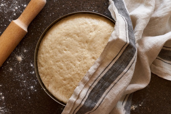 raw yeast dough resting and rising in large metal bowl covering with linen towel - Кулич с изюмом