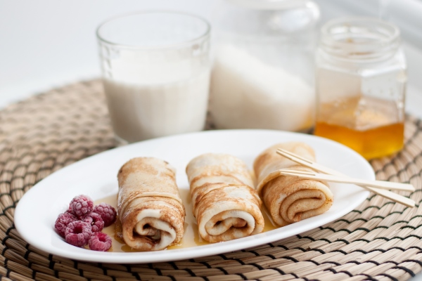 rolled pancakes drizzled with honey and frozen raspberries on a white plate on a wicker napkin - Постные блинчики со сладкой морковью и изюмом