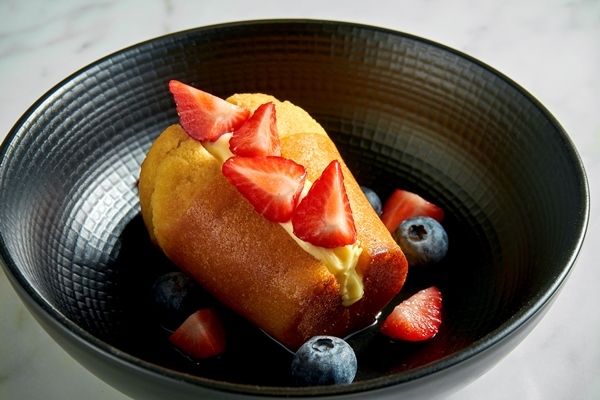 rum baba cake with buttercream strawberry slices and blueberries in a black plate on a white marble table - Баба нежная
