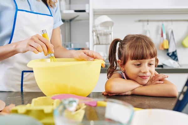 smiling little girl leaning on kitchen counter and watching cartoon on tablet computer when her mother making pancake dough in the morning - Постные гречневые блины на закваске