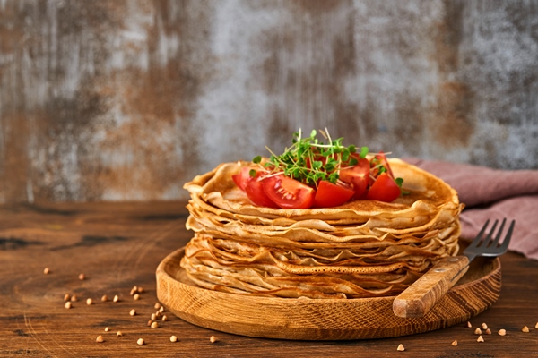stack of gluten free buckwheat flour crepes pancakes with cherry tomatoes and arugula microgreens on wooden plate homemade healthy baking for breakfast - Блинцы пшенично-ржаные постные
