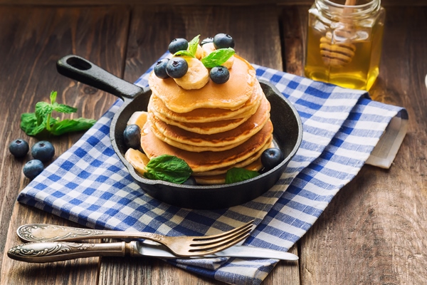 stack of homemade pancakes in iron skillet with blueberries banana and mint leaves on rustic wooden - Постные блинцы без масла