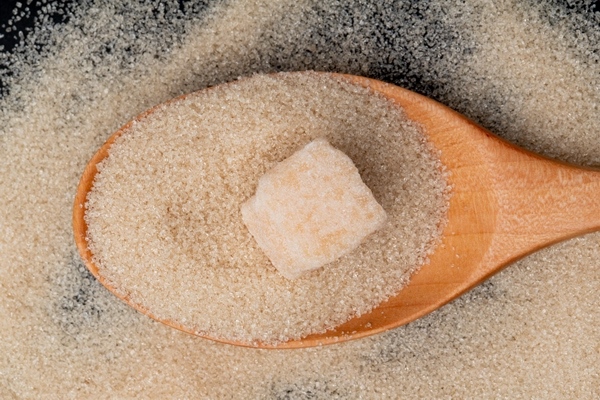 top view of a wooden spoon with brown sugar and sugar cube on granulated sugar background - Консервированная вишня с косточками
