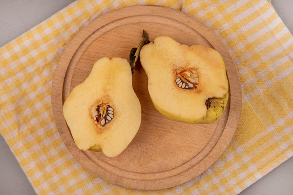 top view of fresh halved quinces on a wooden kitchen board on a yellow checked cloth - Конфитюр из айвы