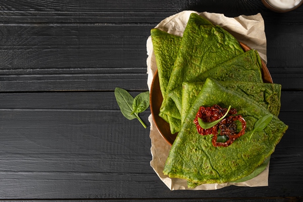 vegetarian green pancakes decorated with dried tomatoes spinach pancakes in a brown plate on dark wooden background copy space - Постные капустные блинчики со шпинатом