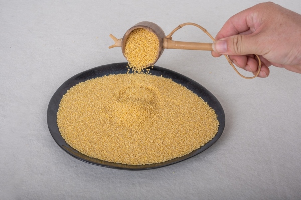 with a spoon in hand pour millet into the bowl containing millet - Постные пшённые дрожжевые блины
