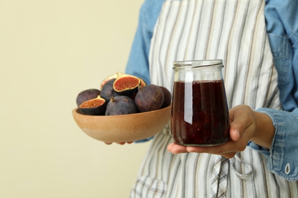 woman in apron holds jar of fig jam and bowl with fig - Библия о пище