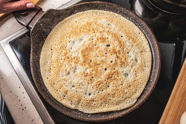 woman is standing at the stove and frying pancakes in a hot pan 1 - Постные блинчики на чае с пряной начинкой