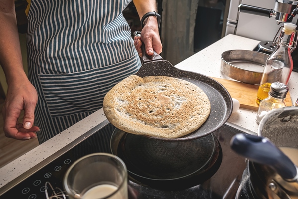 woman is standing at the stove and frying pancakes in a hot pan - Постные блинчики с сиропом из сухофруктов