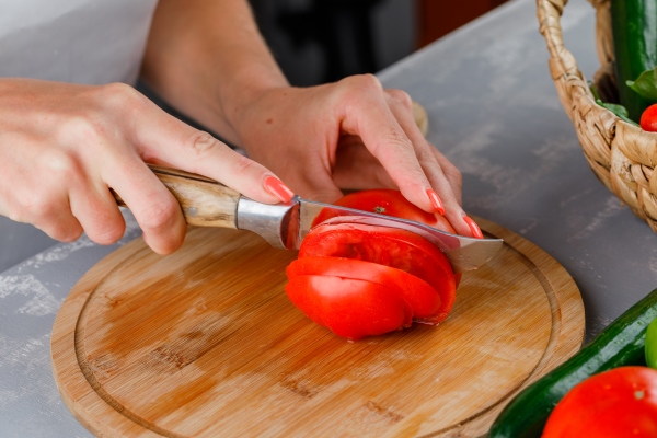woman slicing tomato on a cutting board high angle view on a gray surface - Салат из перца и баклажанов