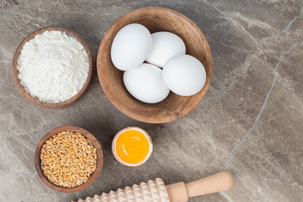 wooden bowl of raw eggs flour and barley on marble surface - Яйца с рисунком и узорами в луковой шелухе