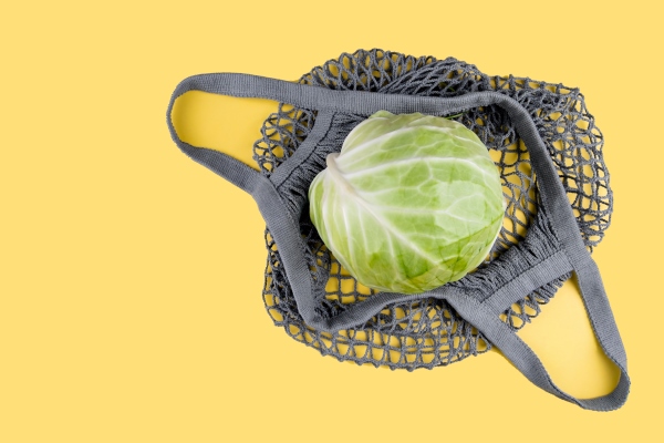 a head of cabbage lies in an ecological string bag on a yellow - Закуска из моркови и капусты с чесноком