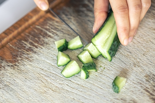 a woman cuts a fresh cucumber on a cutting board - Суп из сныти со свежими огурцами