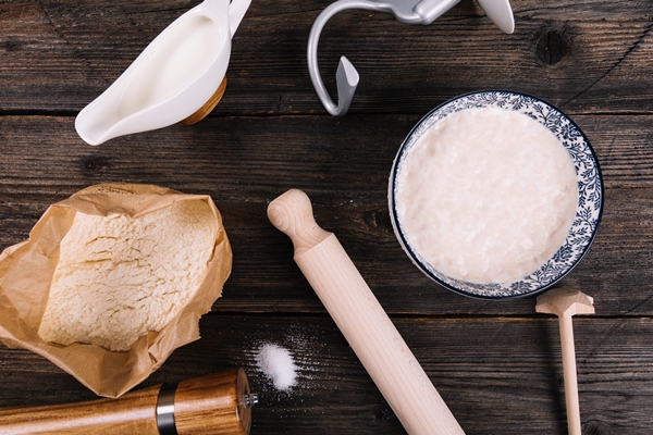 an overhead view of flour milk yeast and peppermill with rolling pin on table - Ватрушки с вареньем или яблоками