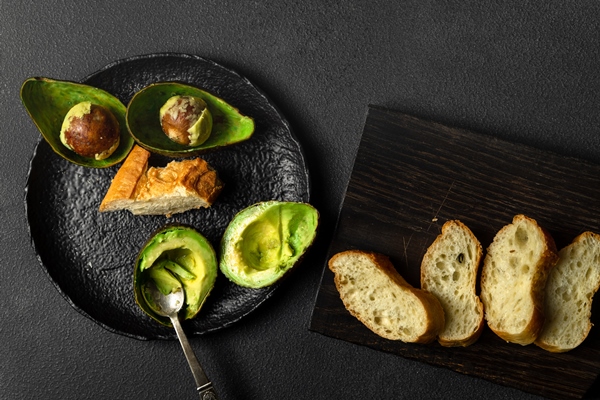 avocado halves bread and spoon on black plate - Перекус "Деликатесный" с креветками
